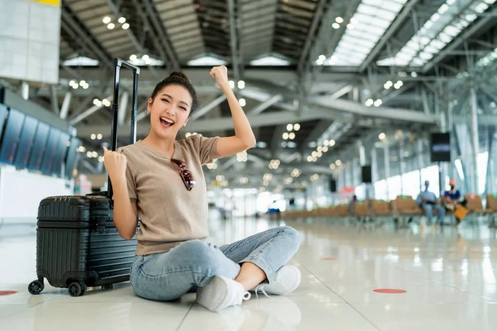 Happy woman sat on the floor in airport terminal — Shutterstock