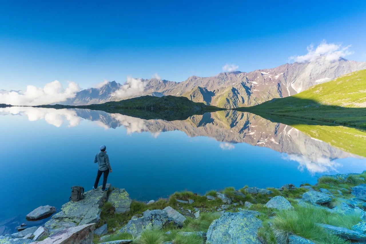 Rear view of hiker on rocks admiring Cima di Pietra Rossa reflected in Lago Nero, Gavia Pass, Valfurva, Valtellina, Lombardy, Italy
