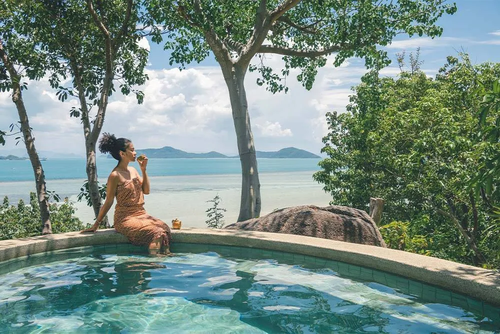Woman sitting on the side of a pool with the coastline in the background — kamalaya.com