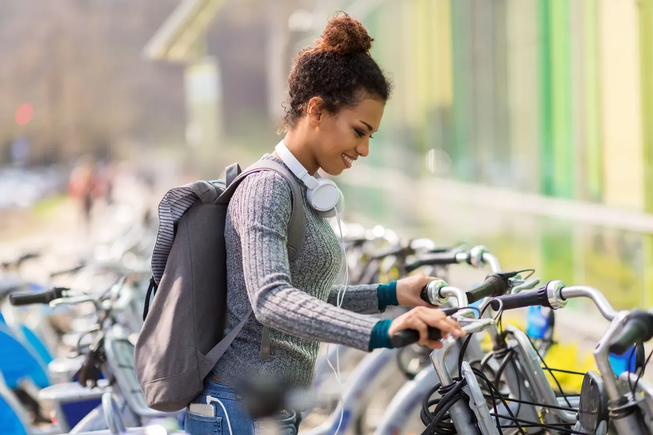 Girl with a backpack renting public bike — Shutterstock