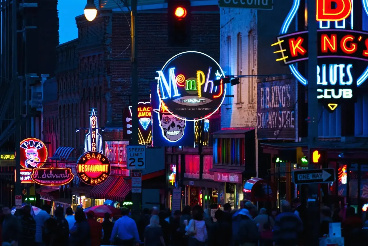 A lively night scene in Memphis, Tennessee, with neon signs lighting up the street, advertising bars, restaurants, and live music venues.
