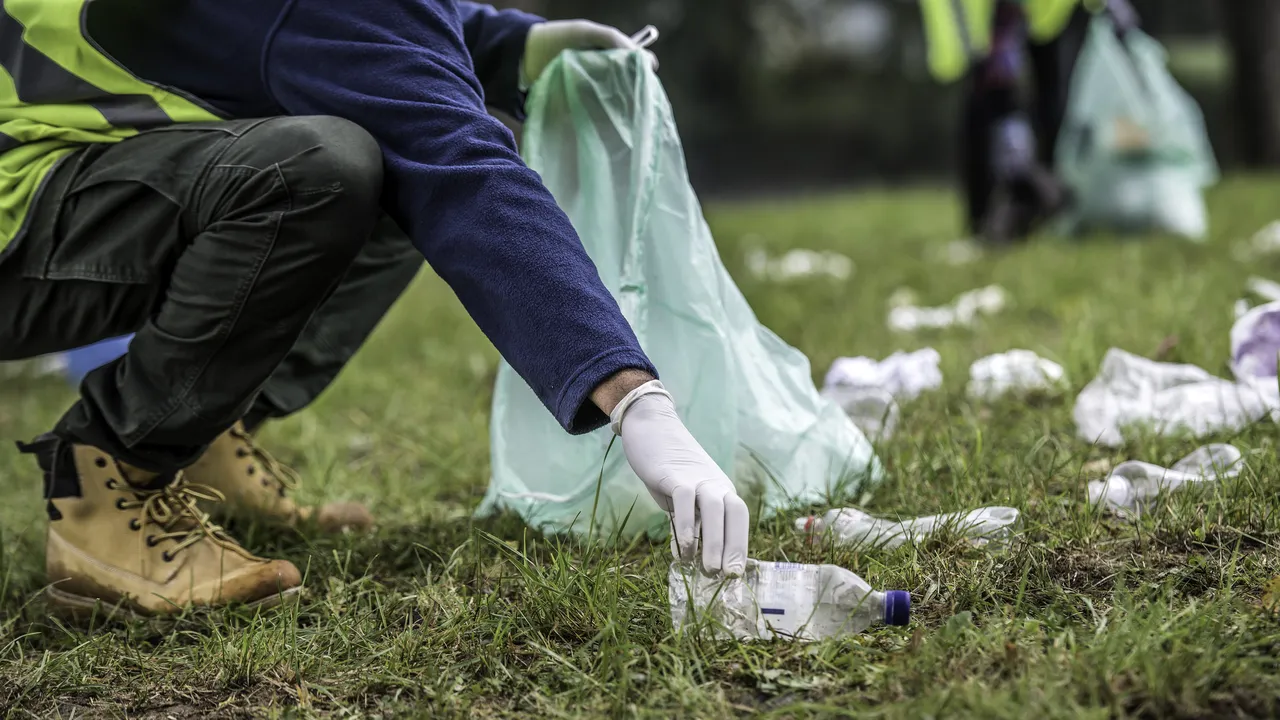 Unrecognizable volunteer picking up a plastic bottle during a park clean-up action.
