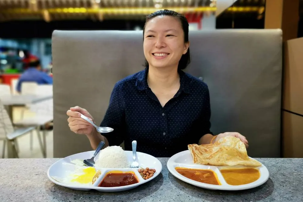 Uśmiechnięta osoba, przed nią talerze z nasi lemak i roti canai