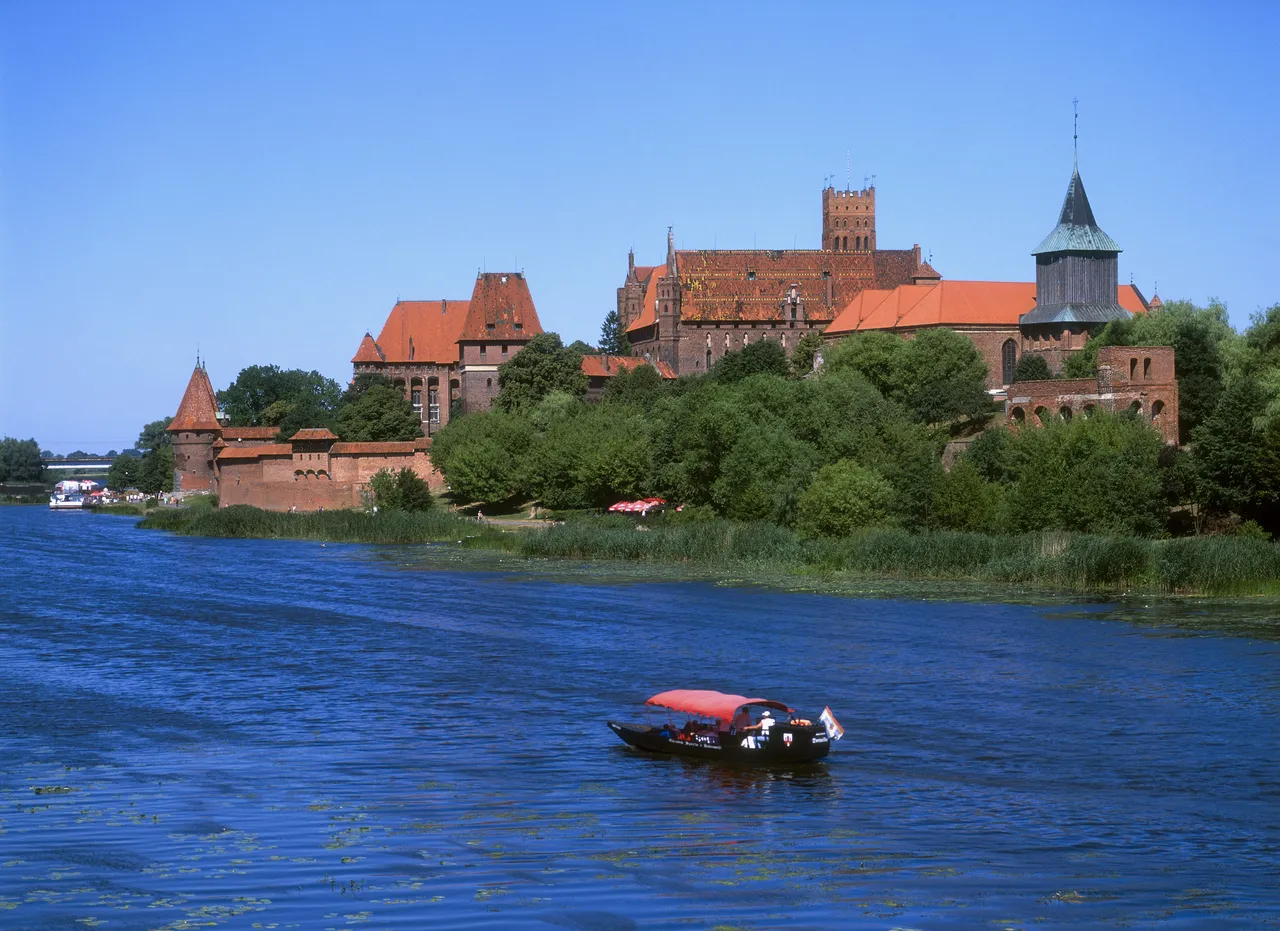 Mała motorówka przepływa obok zamku w Malborku na rzece Nogat, Polska.