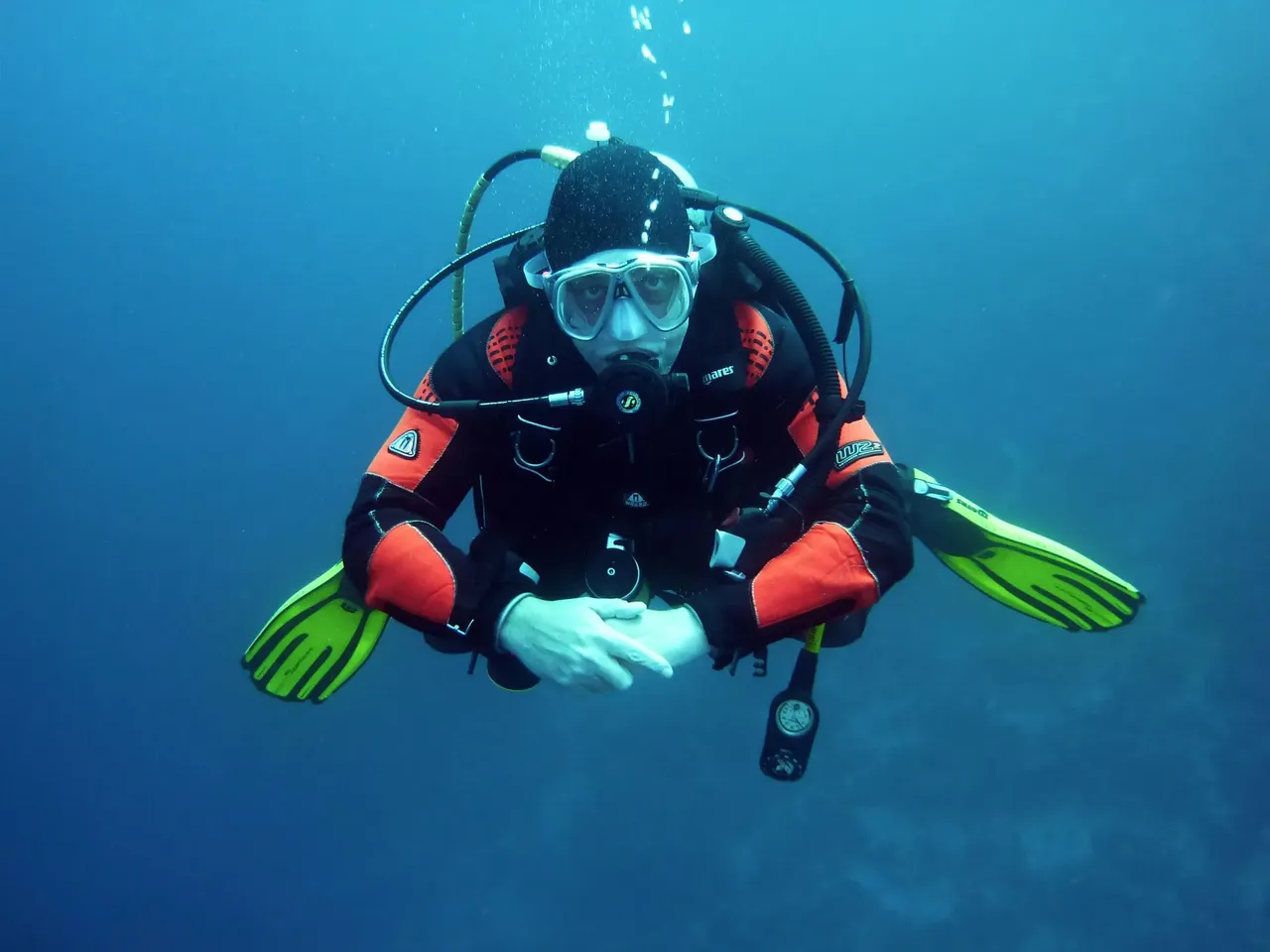 Un instructor enseña habilidades básicas a un buceador principiante durante un curso PADI, con el buceador llevando equipo completo de buceo en aguas poco profundas.