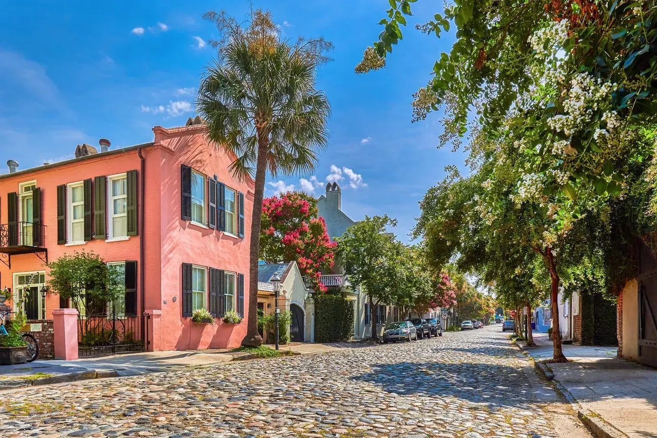A historic cobblestone street in Charleston, South Carolina, lined with charming colonial-style buildings and lush greenery.