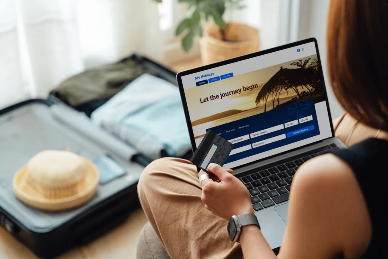 Pohled přes rameno mladé ženy platící kreditní kartou při rezervaci cesty online