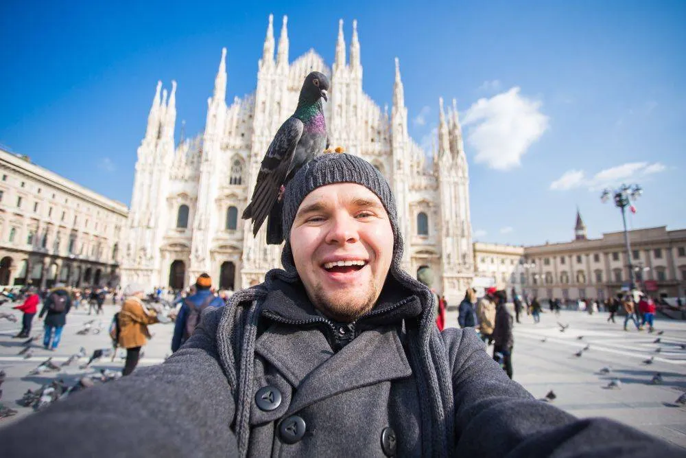 Olaszország, kirándulás és utazás - vicces srác szelfizik galambokkal a milánói Duomo dóm előtt.