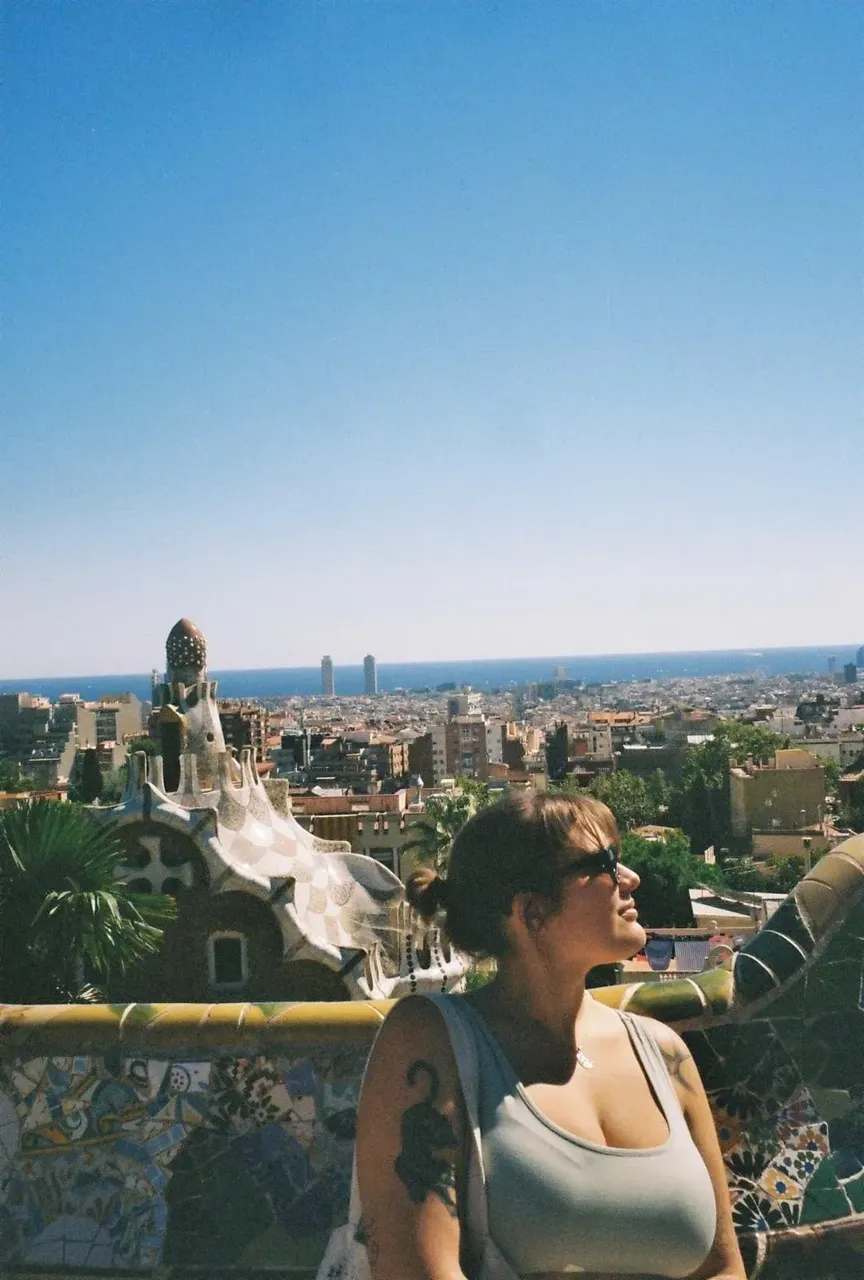 Terasa cu mozaic colorat din Parcul Güell, cu vedere asupra orașului Barcelona, cu băncile sale curbate emblematice și lucrările vibrante din plăci ceramice.