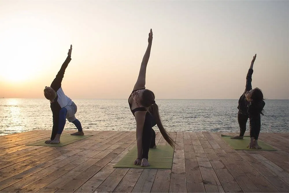 Three people making the same yoga pose on a wooden pier over the sea at dawn — Shutterstock