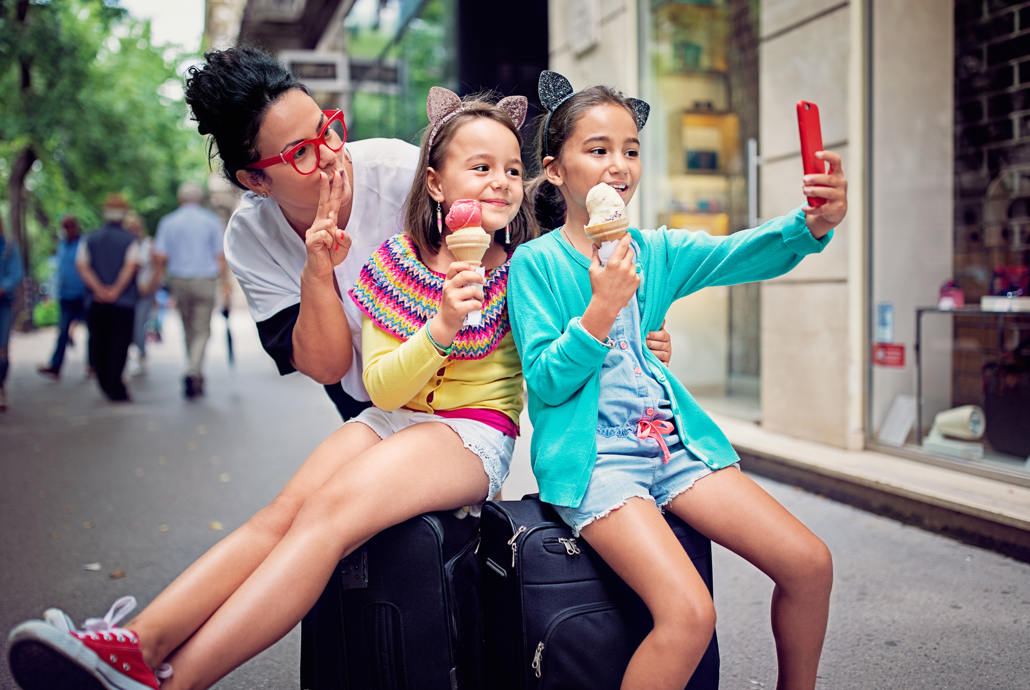 Mother and her two daughters having an ice cream on a lively street, and taking a selfie